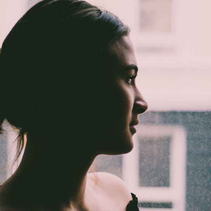 Photo of a young woman looking out a window upon a dreary day