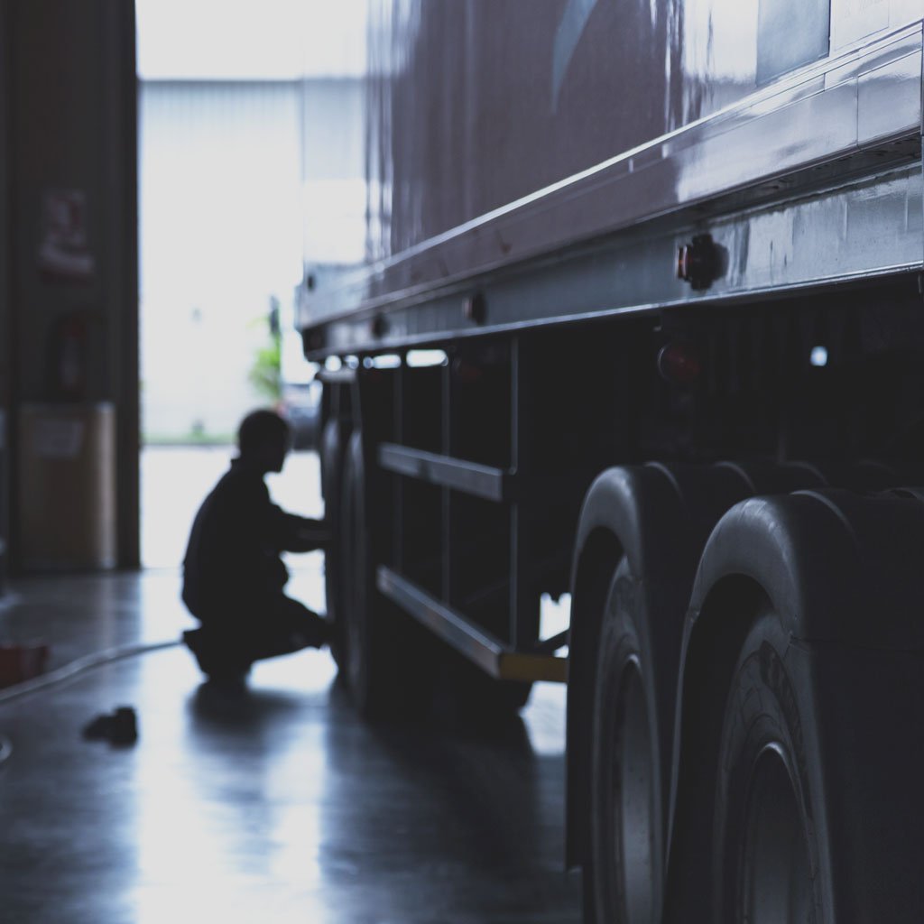Heavily shadowed photo of a male performing maintenance on a semi-truck trailer