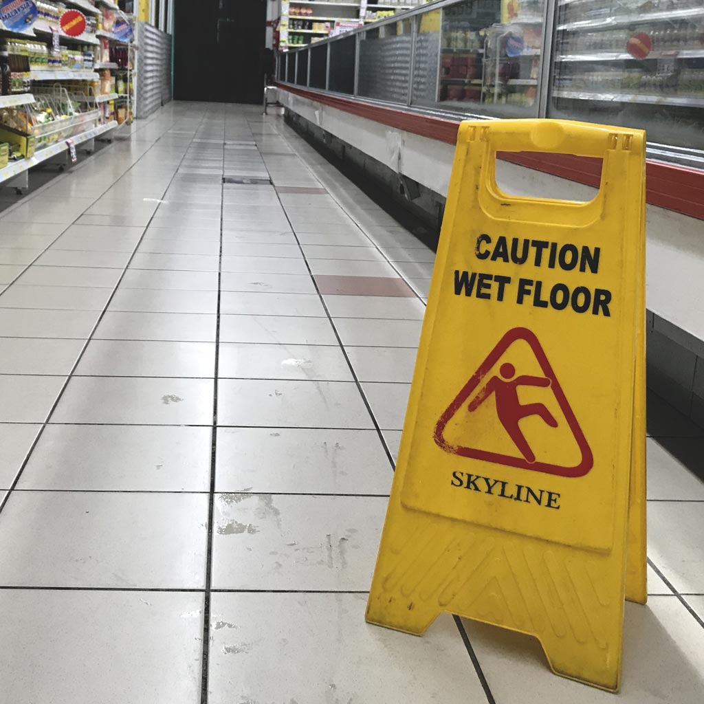 A 'caution wet floor' sign on a dirty grocery store floor